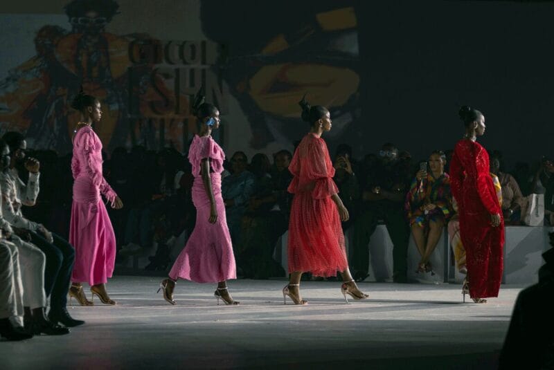 The side profile of four models as they walk down a runway in pink and red dresses.
